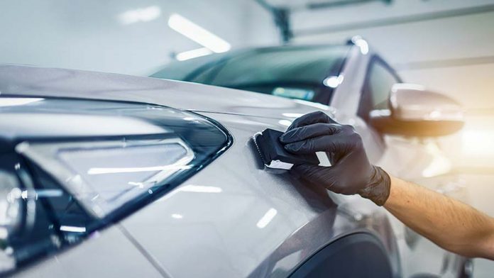 A worker polishes a white sports car with a ceramic coatings brush.