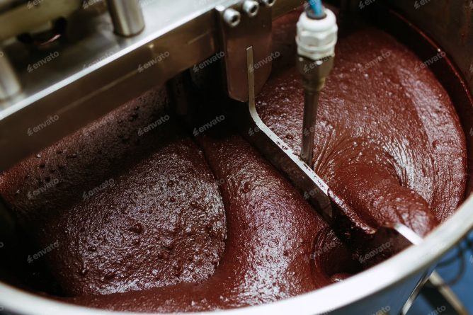 Thick dark brown chocolate being mixed in a factory.